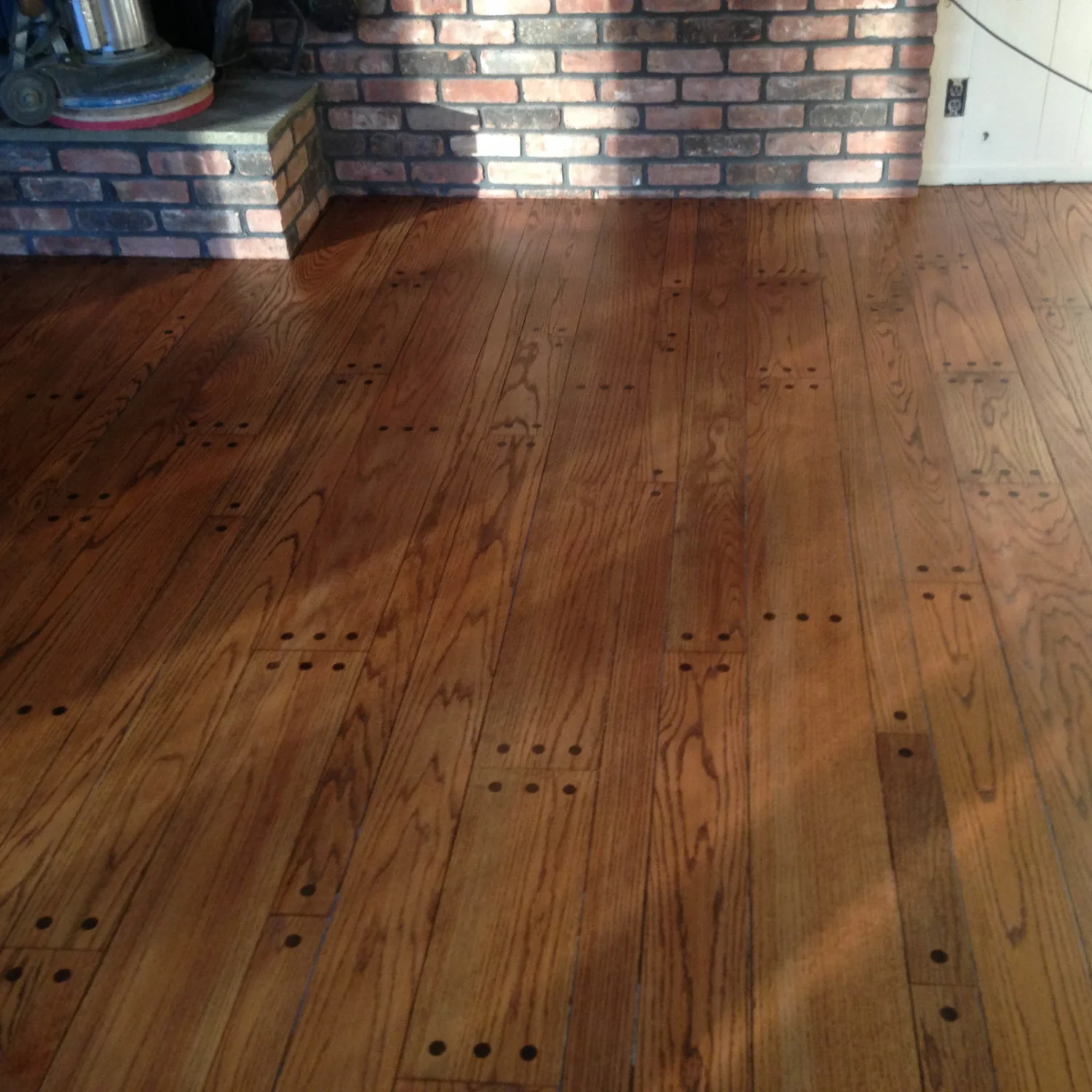 Living room hardwood floor mid-refinish beside a brick fireplace